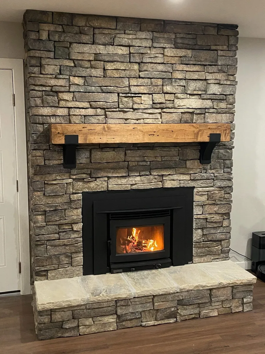 Newly installed wood-burning insert in a floor-to-ceiling stone fireplace with timber mantel